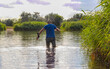 A fisherman using a fishing rod to catch carp in the river while standing in the water. A fisherman among the reeds stands in the river in rubber boots to cast a fishing rod, carp fishing.