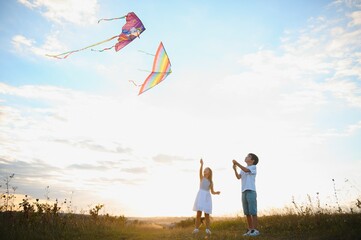 Happy children launch a kite in the field at sunset. Little boy and girl on summer vacation.