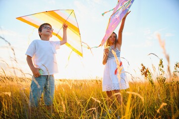 Wall Mural - Happy children launch a kite in the field at sunset. Little boy and girl on summer vacation.