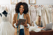 © cherryandbees - A beautiful wedding dress designer holds a tablet and looks at the camera