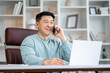 © Ivan - Smiling asian man holding smartphone sitting in office. Digital technology applications and solutions for business development. Copy space