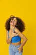 © SHOTPRIME STUDIO - Woman with curly afro hair in a blue T-shirt on a yellow background dancing flying hair with sunglasses yellow, hand signs, look into the camera, smile with teeth and happiness, copy space