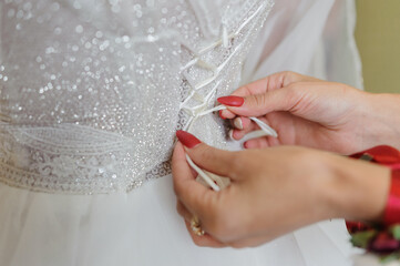 Wall Mural - Bridesmaids tie a bow on the wedding dress. Preparing the bride. Morning of the bride