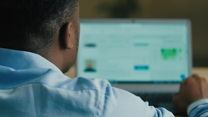 Over shoulder back view unrecognizable African American man guy businessman freelancer employee search social media business network look at laptop screen scrolling website on computer in home office