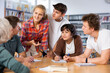 © JackF - Positive teenage students working and discussing in groups in college library