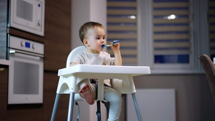 Wall Mural - Relaxed little kid eating fruit puree from plastic tube. Sweet kid enjoying baby food from pack. Low angle view.