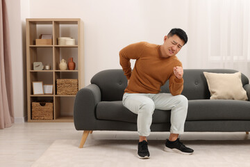 Poster - Asian man suffering from back pain on sofa indoors