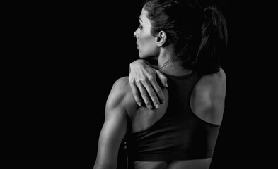 Wall Mural - Female sporty muscular model with ponytail doing correction massage holding the hand the low back on dark shadow black background with empty copy space. Back view.