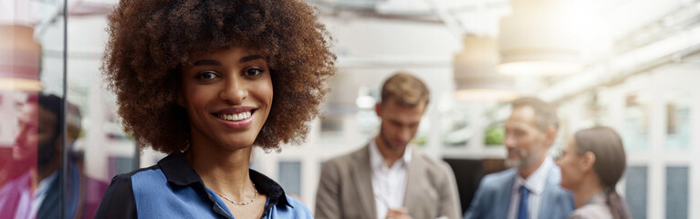 Wall Mural - Smiling african businesswoman with laptop standing in modern office on colleagues background