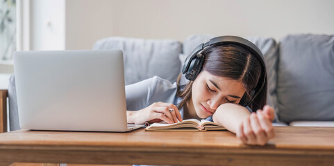 Wall Mural - Tired teenage asian female student fell asleep at her desk, resting her head on her hand, during a lecture in home, taking a break, closed her eyes and relaxing