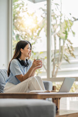 Wall Mural - girl wearing headphones watching movies listening to music on laptop on the sofa at home on vacation with a cup of coffee