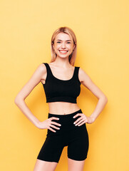 Young beautiful smiling blond female in black summer cycling shorts clothes. Sexy carefree woman posing near yellow wall in studio. Positive model having fun indoors. Cheerful and happy