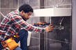 © Jordan C/peopleimages.com - Black man, plumber and maintenance in bathroom, fixing sink pipe with wrench and plumbing industry. Manual labor, male with focus and trade, handyman doing repairs with tools on home renovation