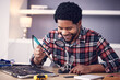 Black man, technician and fixing computer circuit board in hardware, soldering iron tools or tech repair. Maintenance, magnifying glass or electrical fix with happy male working on device motherboard