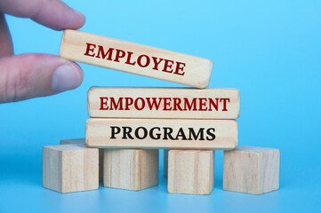 Hand placing employee empowerment programs text on wooden blocks with blue cover background. Employee empowerment concept.