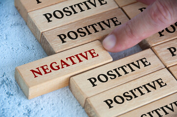 finger pushing negative text on wooden block from the rest of the wooden blocks with positive text. 