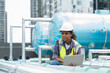 © amorn - Female engineer worker using laptop computer inspecting quality sewer pipes at rooftop of building. African American woman engineer working, checking or maintenance sewer pipes at construction site