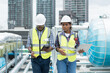 © amorn - Male and female engineer worker working with laptop computer discuss and inspecting structure of building at rooftop of building at construction site