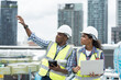 © amorn - Male and female engineer worker working with laptop computer discuss and inspecting structure of building at rooftop of building at construction site