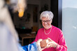 © Studio Marmellata - Positive elderly gray haired woman in glasses and pink sweater receiving package from courier while standing at doorway