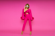 High Fashion Model. Elegant Woman Is Wearing Pink Feather  Jacket, Trousers And High Heels On Pink Background.  Chic Female Model Posing In Stylish Luxury Outfit.