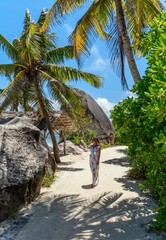 Wall Mural - Girl wearing sun dress and hat walking on sandy beach with palm trees