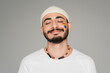 © LIGHTFIELD STUDIOS - portrait of smiling gay man in hat with lgbt flag on cheek standing isolated on grey.