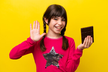 Wall Mural - Little caucasian girl with chocolat isolated on yellow background saluting with hand with happy expression