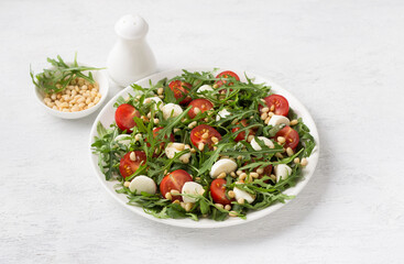 Wall Mural - Salad with arugula, cherry tomatoes, mini mozzarella and pine nuts on a light gray background. Delicious homemade traditional food