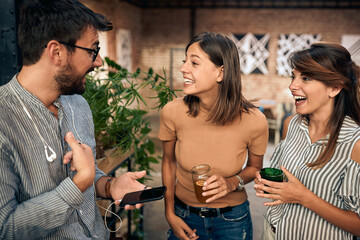 Wall Mural - Cheerful friends at the bar standing and having a fun conversation. Two girls and a guy talking.