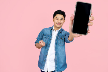 Cheerfull Asian man jumping and smiling in air with showing cellphone blank screen with empty space for mobile app on screen. Isolated in studio light pink background. Creative collage.
