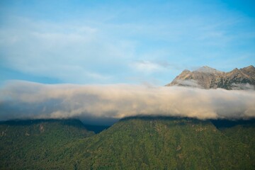 Sticker - Majestic mountain range illuminated by the sun, with light clouds scattered across the landscape