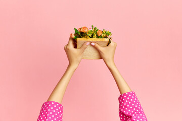 Portrait with female hands holding sandwich with flowers inside on pink studio background. Diet for weight loss