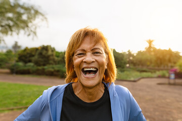 Happy senior Latin woman having fun smiling on camera after training activity in a public park