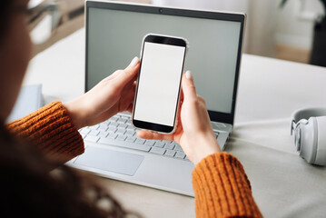 Over shoulder view of woman holding mobile phone with white blank mock up cellular screen applications working using cell phone. Cellphone display mock up for advertising apps concept.