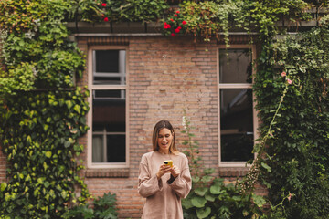 Wall Mural - Portrait of a beautiful smiling woman using a mobile phone outdoors. Girl holding smartphone and reading text message. Smiling woman using mobile phone outside.