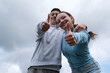 © Oleksandra - against the backdrop of a stormy cloudy sky boys teenage girls lean over showing thumbs up approval advertising beautiful real children adolescence social benefits assistance social service school