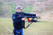 © Olga - Instructor man, gun and learning to shoot outdoor at shooting range for target training. Safety and security with hand teaching person sport game