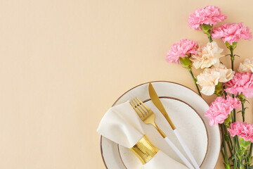 Wall Mural - Stylish Mother's Day table setting concept. Top view photo of plate cutlery knife fork napkin with ring  and bouquet carnations on light beige background. Flat lay with space for greeting or advert