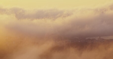 Wall Mural - aerial view through sunny clouds over the city and sea, mystic foggy sunrise above the earth, citysc