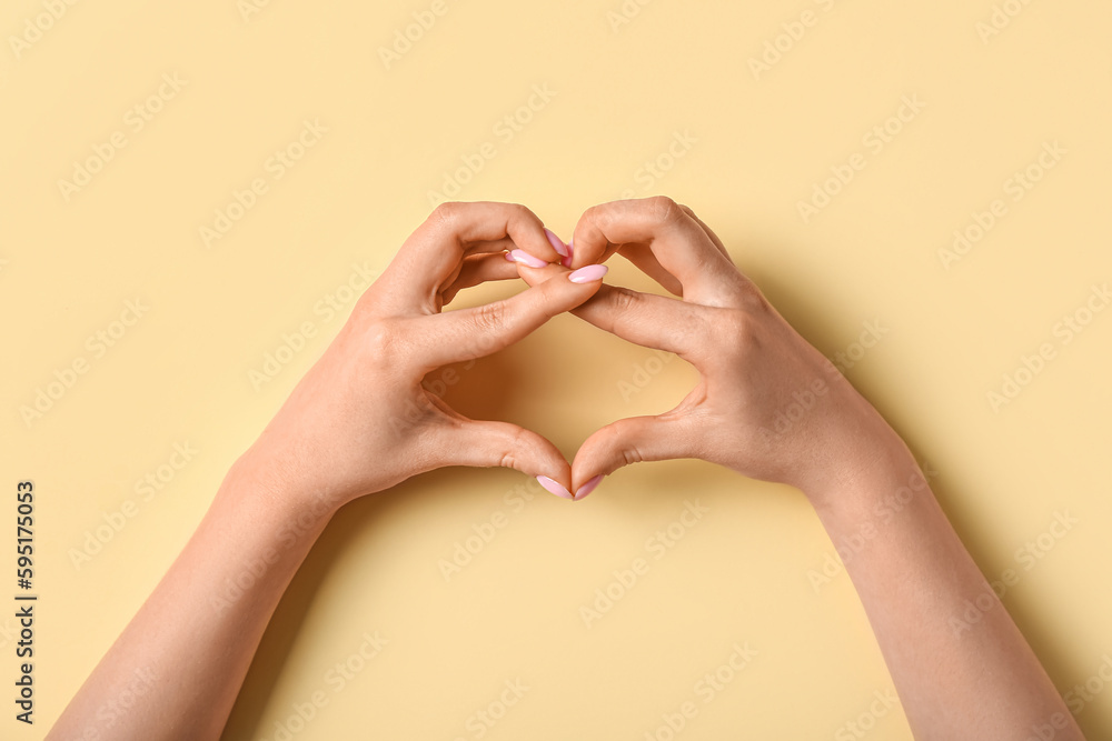 Woman making heart with her hands on beige background