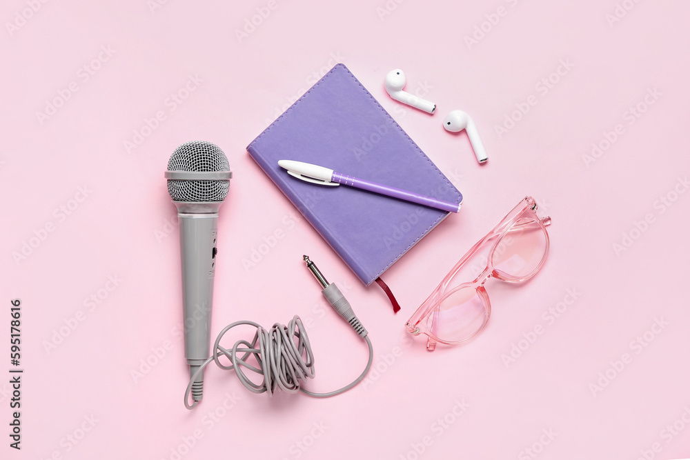 Notebook with microphone, eyeglasses and earphones on pink background