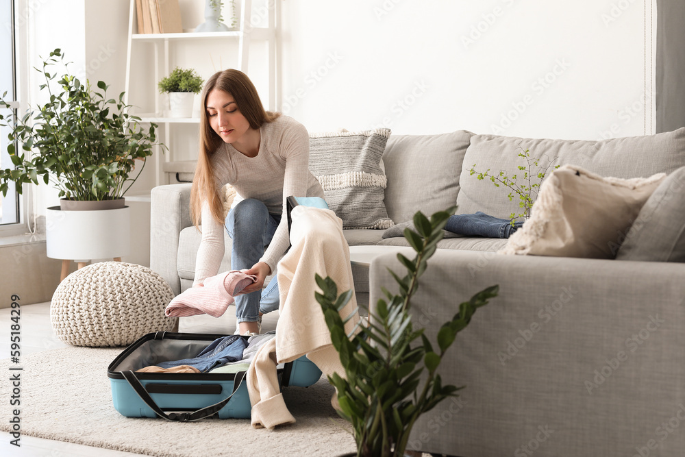 Young woman putting folded clothes into suitcase at home