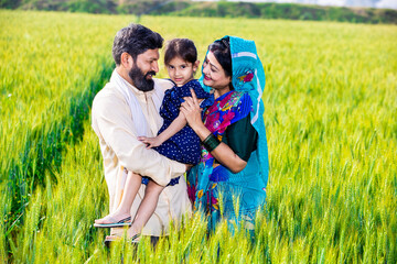 Wall Mural - Portrait of happy young indian farmer family standing at wheat agriculture field in bright sunny day. Parent with child daughter,Rural india concept.