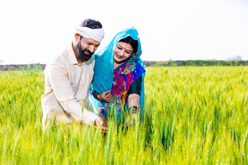 Wall Mural - Happy young indian farmer couple touching wheat crop standing at agriculture field in bright sunny day. Copy space. Rural india concept.