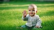 © Collab Media - Closeup of happy baby waving hello sitting on green grass lawn. Generative AI