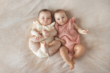 Top View Of Two Cute Baby Twin Girls 6 Month Old Lying Together On Comfortable And Soft Bed With Beige Cotton Blanket At Home

