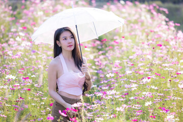 Wall Mural - Beautiful woman happy traveler holding umbrella and walking in the flowers garden. Young woman smile and relaxing in flower garden. Woman's hand touching and enjoying cosmos flowers.Travel concept.