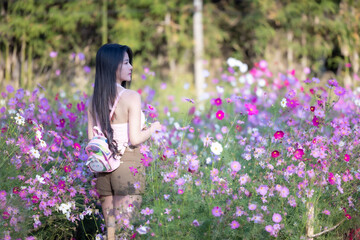 Wall Mural - Beautiful woman happy traveler walking in the flowers garden. Young woman smile and relaxing with happy  around outdoor garden. Woman's hand touching and enjoying beauty cosmos flowers.Travel concept.