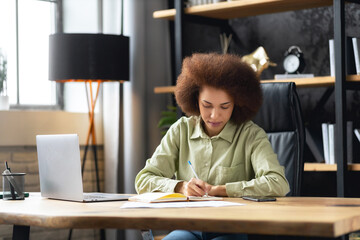 Professional African American business woman worker employee sitting at desk working on laptop in modern office. Focused woman concentrated working on a project